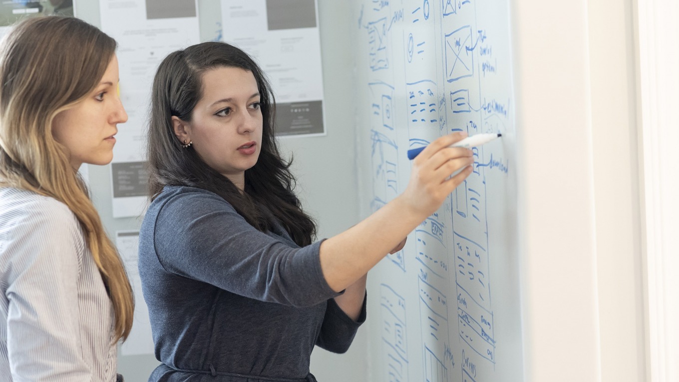 Two women writing on a white board and brainstorming